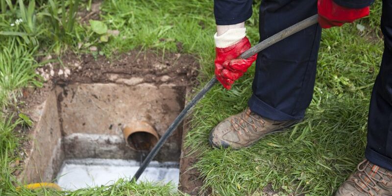 Man with ground open unblocking a drain with a tool Trenchless Water Line Replacement in Odessa, Texas
