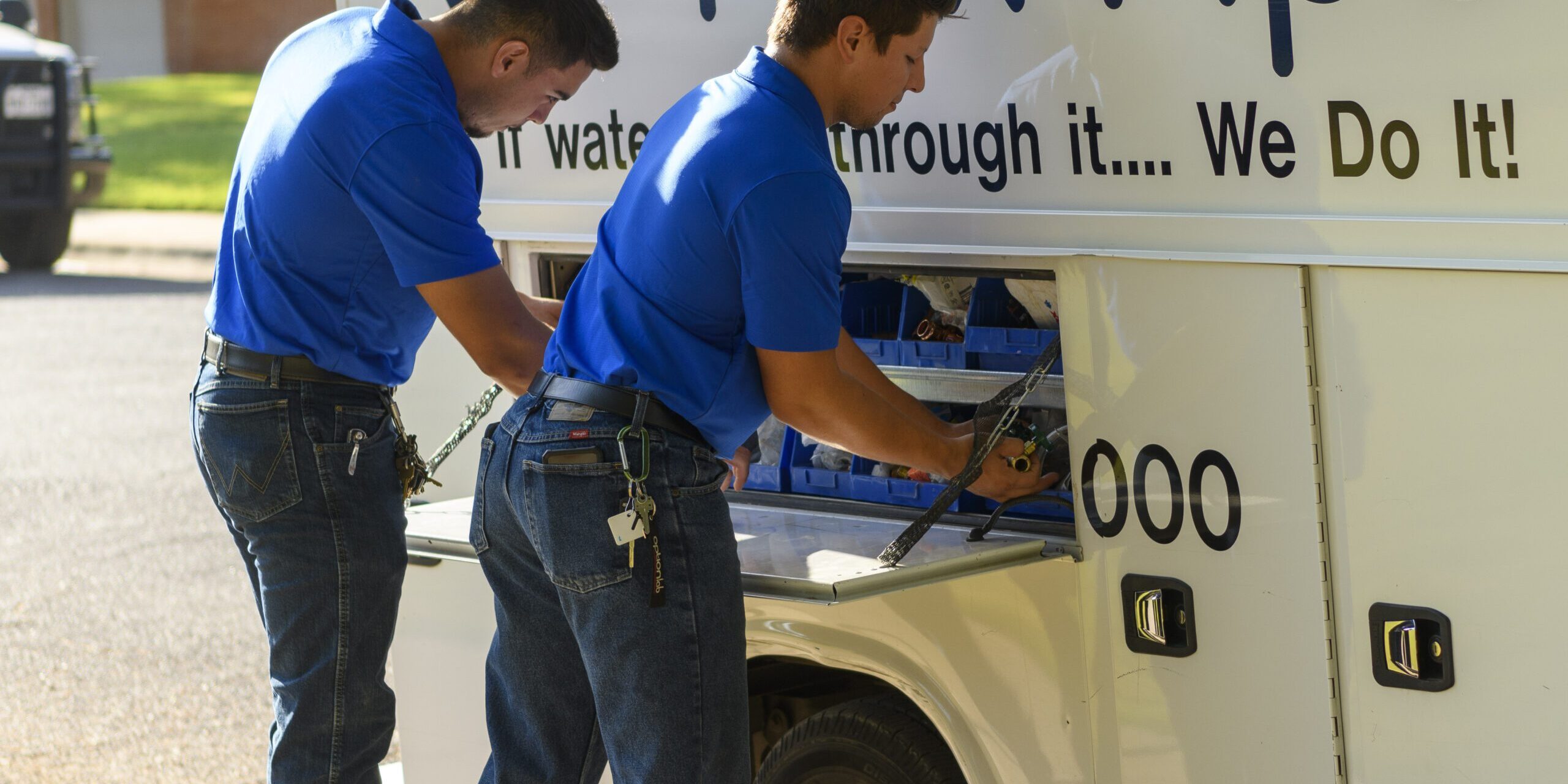 Two technicians in blue shirts accessing tools from a service vehicle, representing I Fix Pipe's plumbing services and trenchless pipe repair solutions.