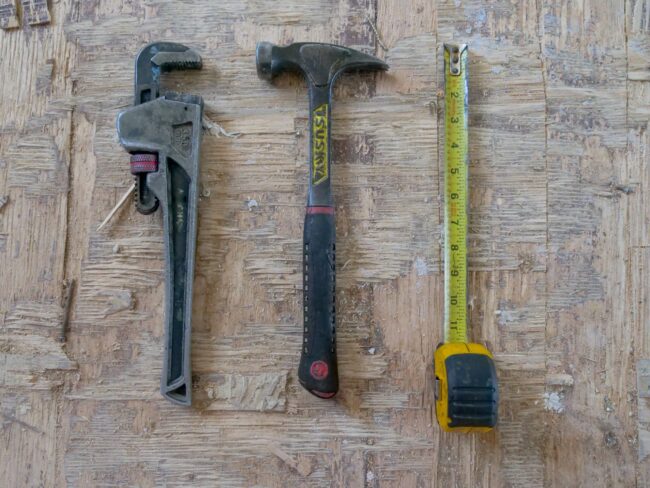 Adjustable wrench, hammer, and tape measure on wooden surface, representing essential plumbing tools for home repairs and maintenance.