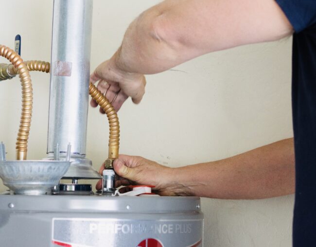 Adult male making adjustments and tightening connections on a gas water heater, illustrating plumbing repair services.