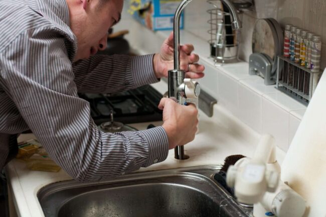 Plumber repairing a kitchen faucet, demonstrating leak detection and plumbing skills in a home setting.