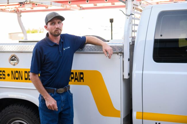 Man in a blue I Fix Pipe shirt standing next to a service truck with "SEWER REPAIR" text, representing plumbing services and sewer pipe repair solutions.