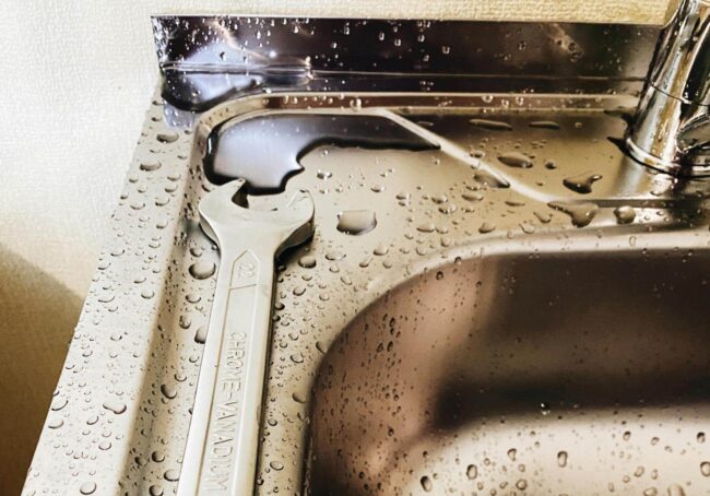 Wrench on a wet stainless steel sink surface, highlighting plumbing repairs and leak detection themes.