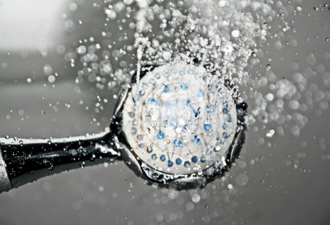 Showerhead with water spraying, illustrating plumbing issues related to water heating and maintenance.