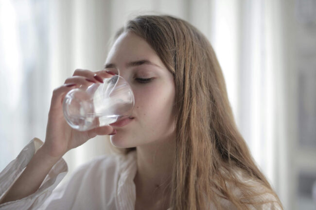 Young woman drinking water from a glass, highlighting the importance of clean water for plumbing health.