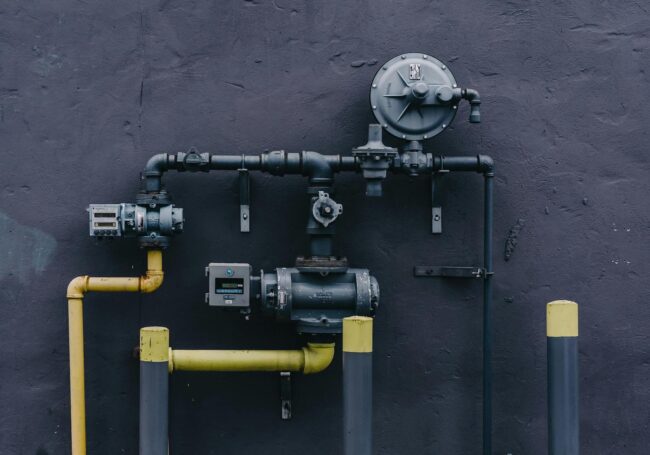 Gas line infrastructure featuring black and yellow pipes, a pressure regulator, and a meter, relevant to plumbing services and gas line repairs.