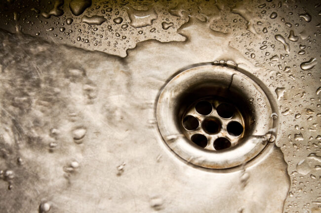 Close-up of a stainless steel sink drain with water droplets, illustrating plumbing issues relevant to homeowners in Odessa, Texas.