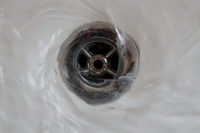 Drain with water swirling around, illustrating a common plumbing issue related to hair clogs.