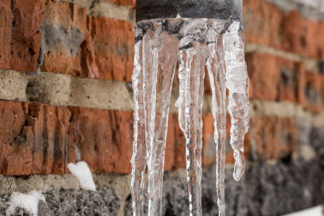 an exposed outdoor pipe with icicles hanging from it