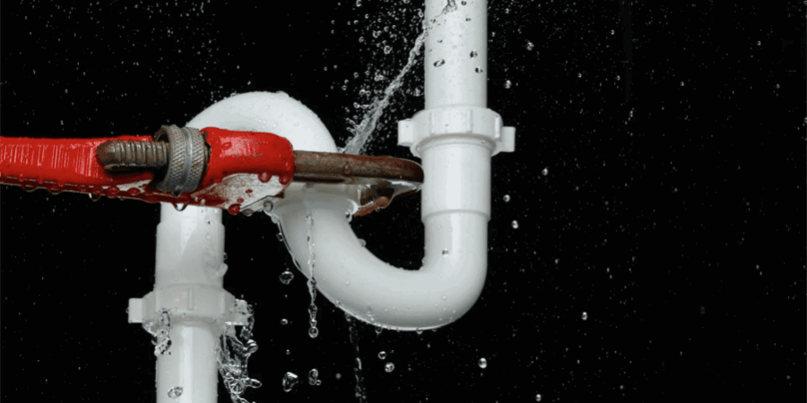 Red pipe wrench tightening a white PVC pipe with water spraying, illustrating plumbing maintenance and leak prevention.