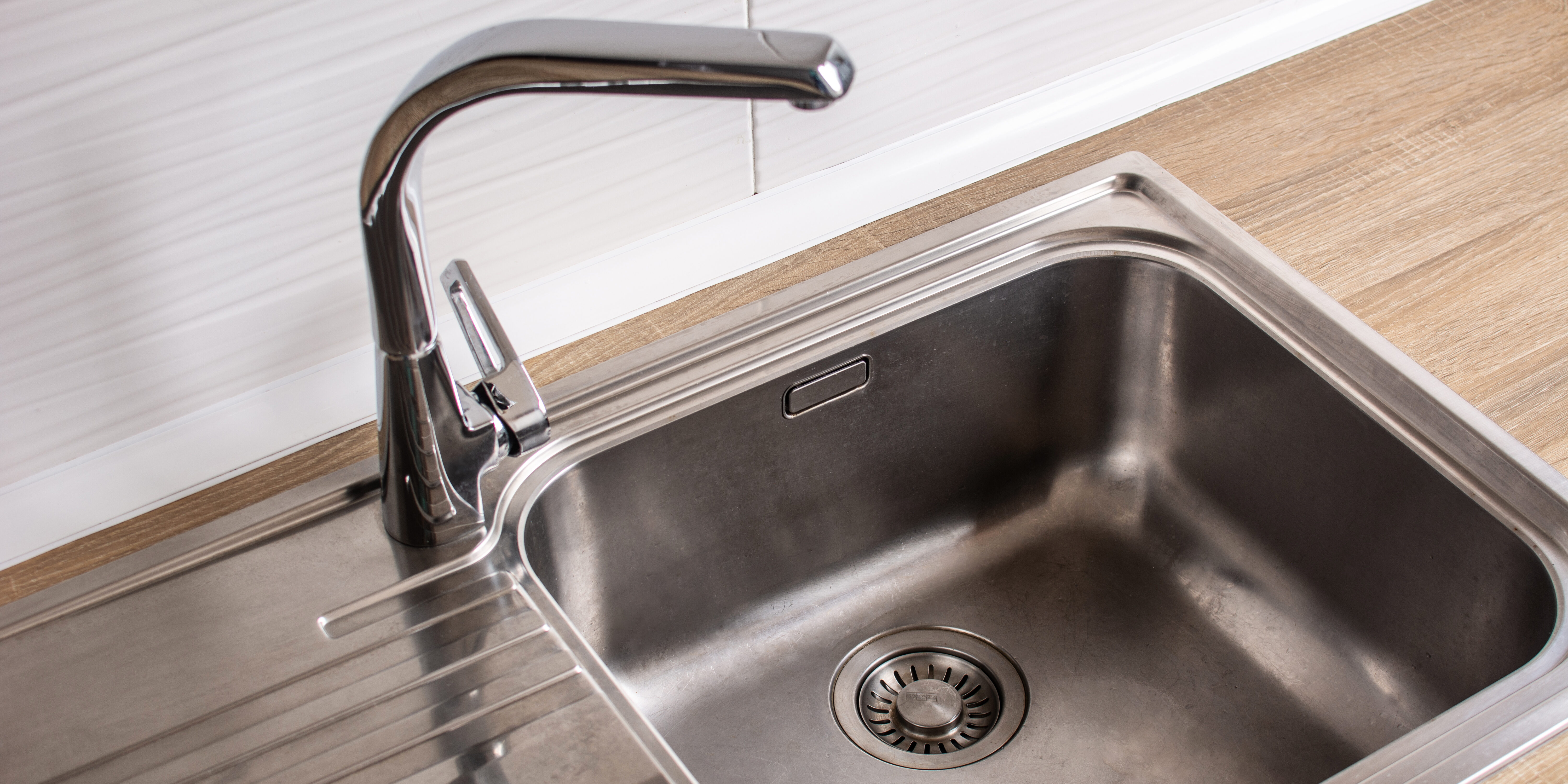 A stainless steel kitchen sink, focused on the drain