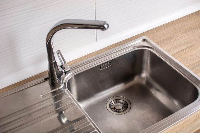 A stainless steel kitchen sink, focused on the drain